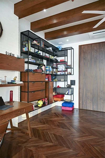 DESIGN CHRONICLES Modern library and study corner featuring a wooden desk, open shelving with black metal accents, colorful cushions, and neatly organized books and decor items.