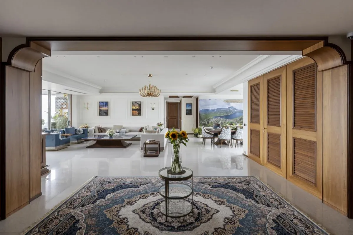Entrance foyer of The Colonial Home by 7Nirvana, with Burma teak louvred doors, a handwoven carpet and a view into the sea-facing living room in Mumbai