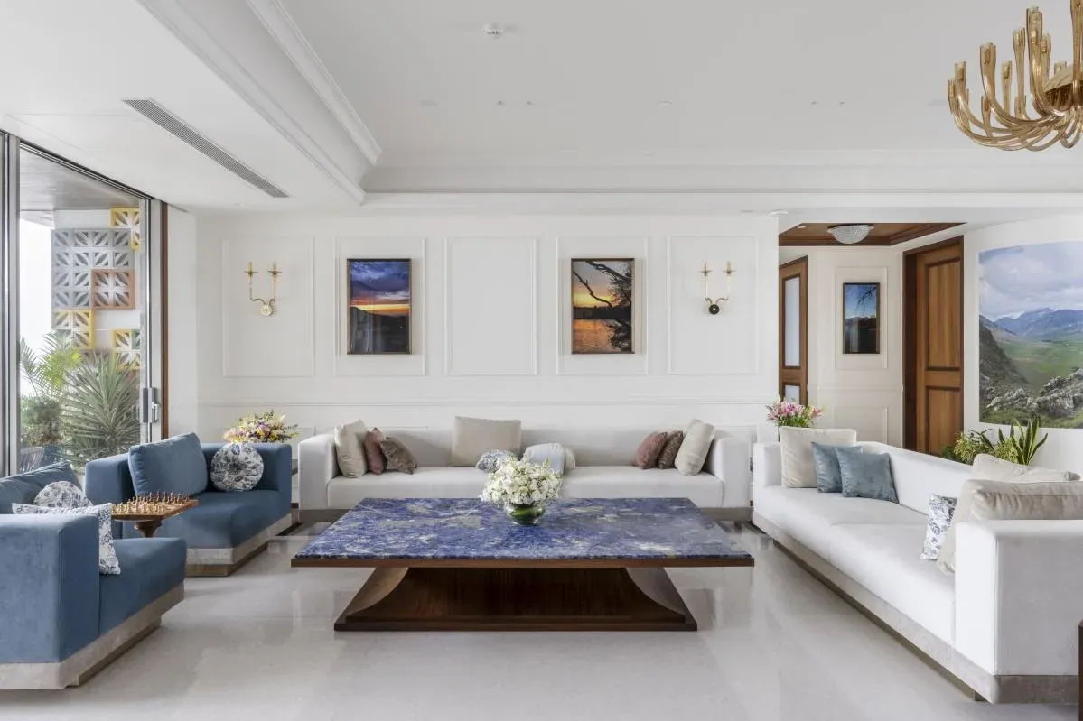 Living room of The Colonial Home by 7Nirvana, with blue and white sofas, a marble coffee table and the client's travel photography on panelled walls